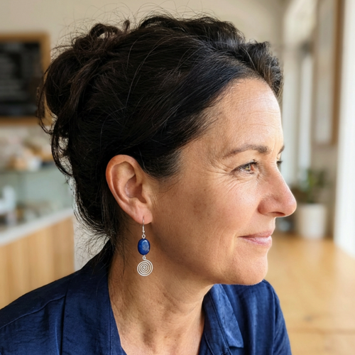 Woman wearing blue earrings with silver spirals in a blurred indoor setting