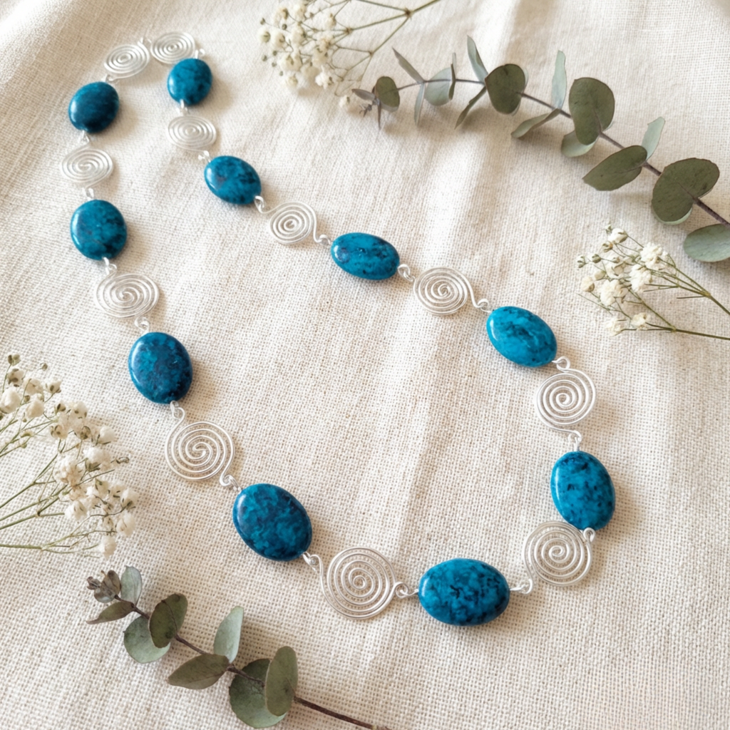 Necklace with blue beads and silver spiral accents on a beige fabric background