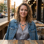 Woman sitting at an outdoor cafe table with a city street background earing a denim jacket and an Azurite and silver spiral necklace