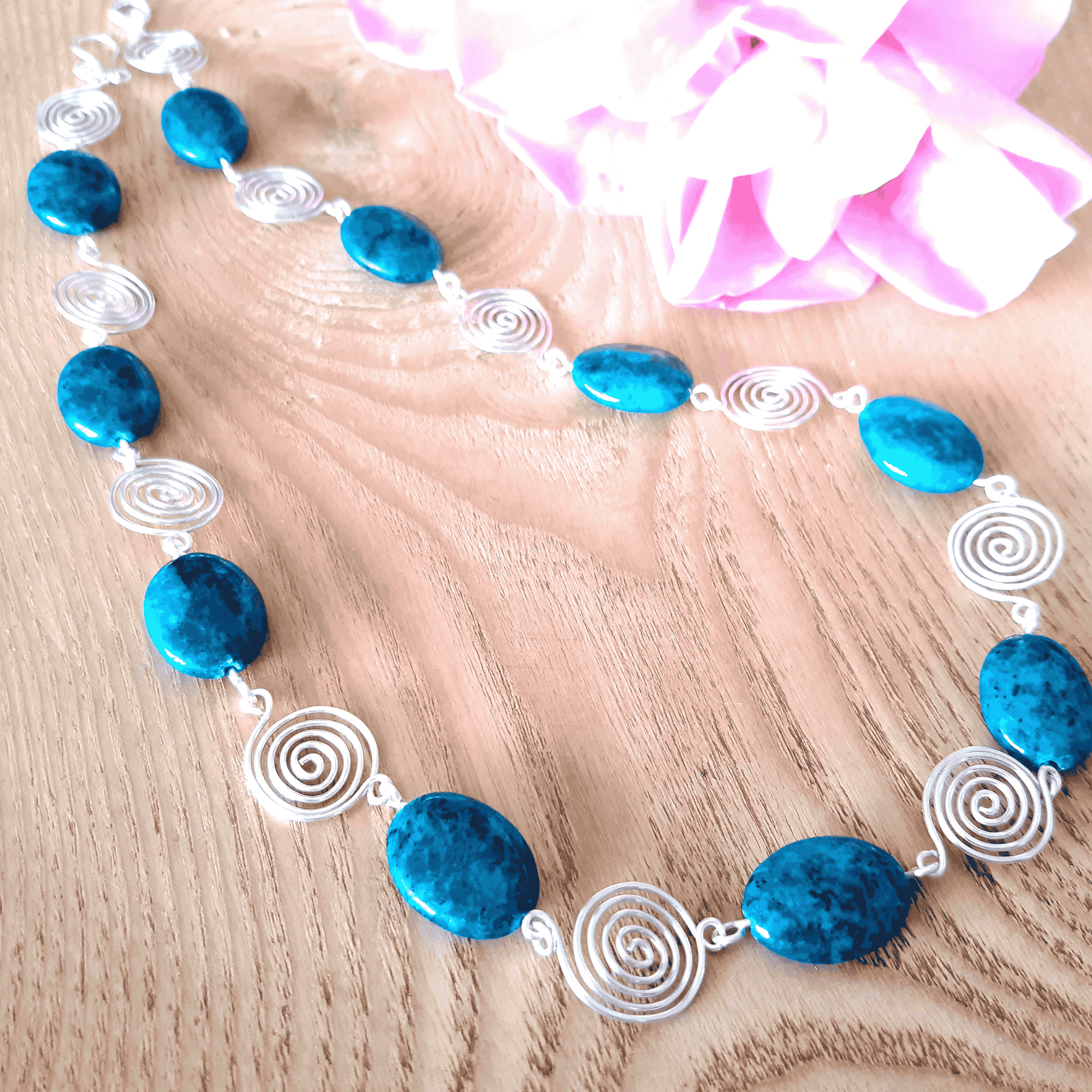 Necklace with blue beads and silver spiral accents on a wooden surface