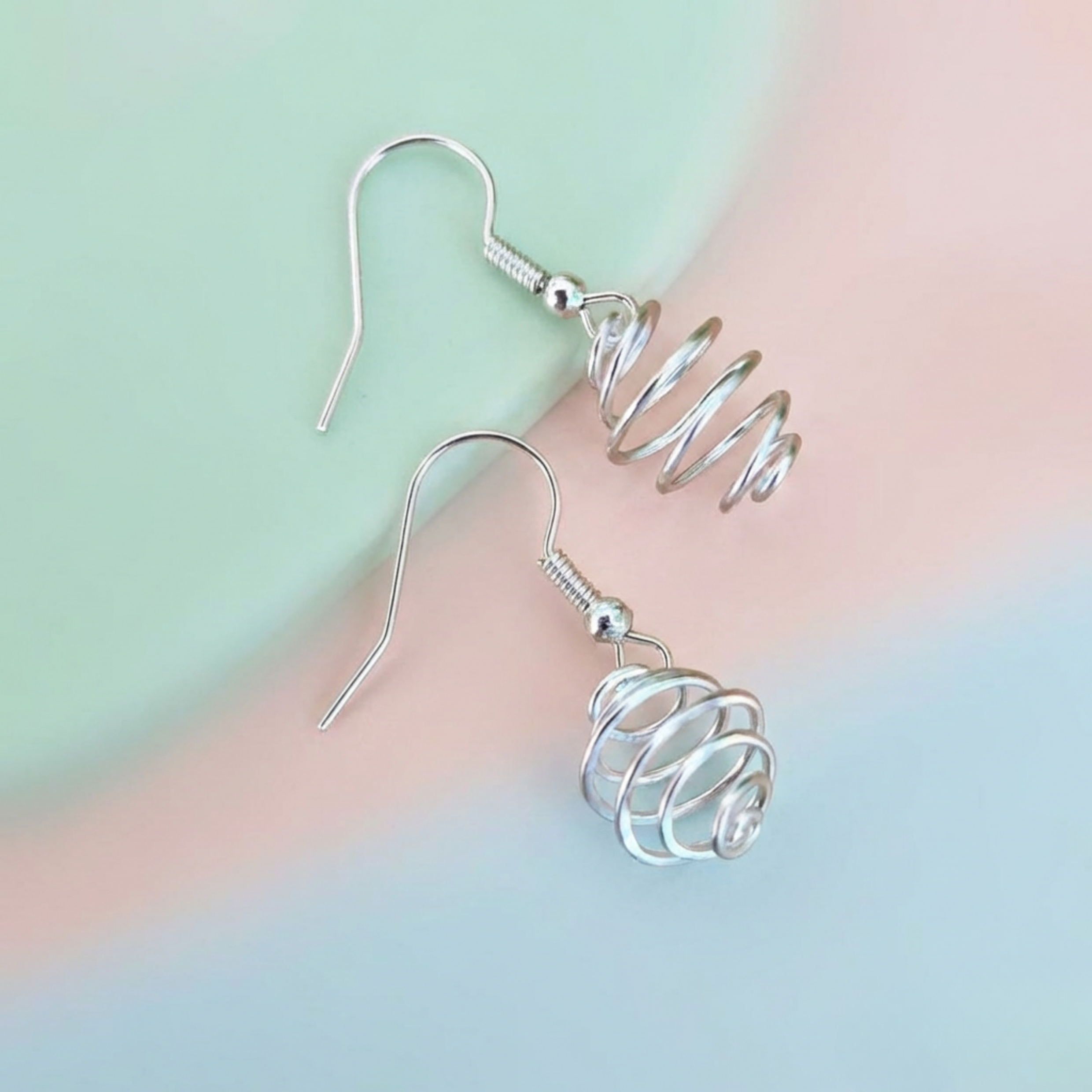 Silver spiral earrings on a pastel gradient background