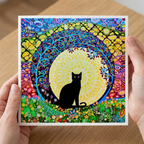 Colourful artwork greeting card of a black cat in a mandala design held by hands on a wooden surface.