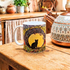 Mug with a cat design on a wooden table next to a decorative teapot.