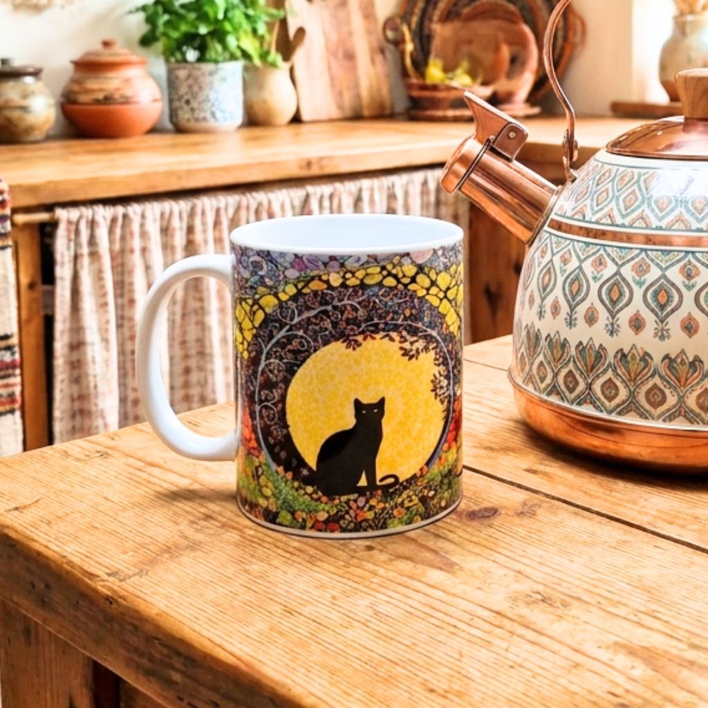 Mug with a cat design on a wooden table next to a decorative teapot.