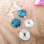 Pair of earrings with blue and brown marbled beads and silver spiral designs on a wooden surface.