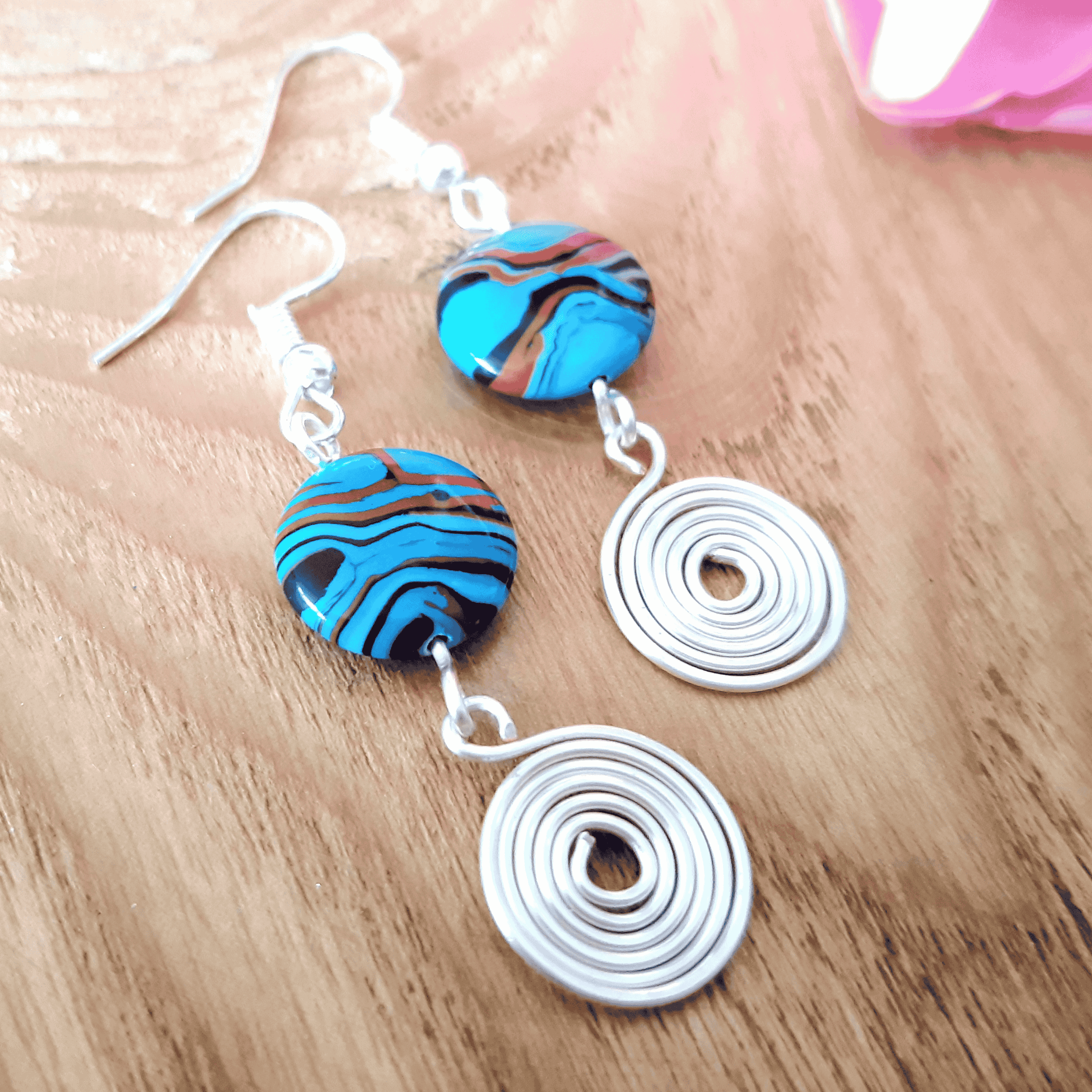 Pair of earrings with blue and brown marbled beads and silver spiral designs on a wooden surface.