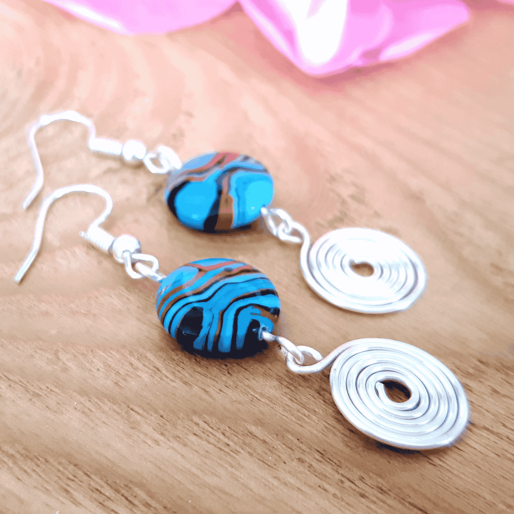 Pair of earrings with blue and orange marbled beads on a wooden surface