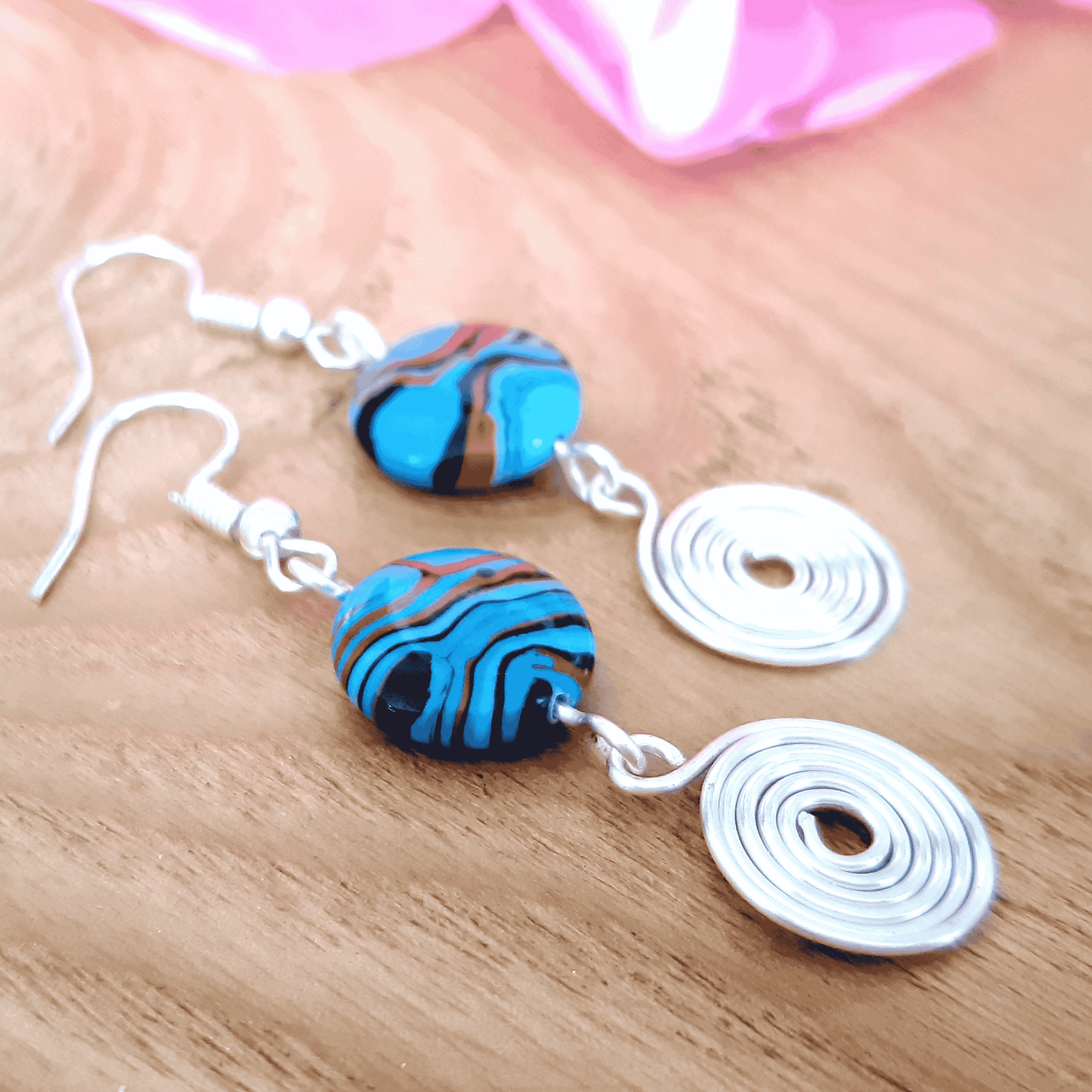 Pair of earrings with blue and orange marbled beads on a wooden surface