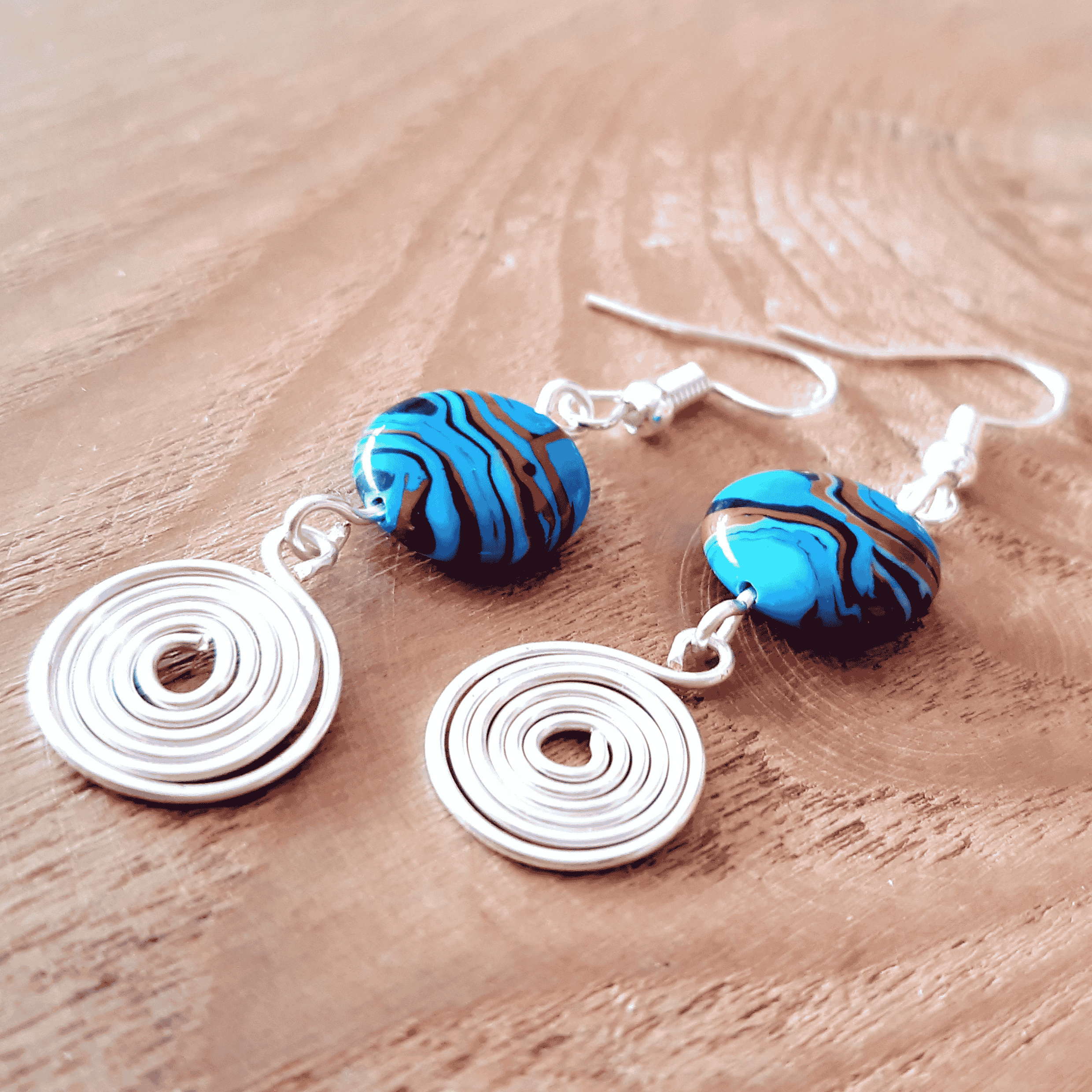 Pair of earrings with blue and brown marbled beads on a wooden surface