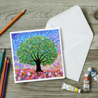 Colourful tree artwork on a card with an envelope and art supplies on a wooden surface