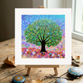 Colourful abstract tree painting on a wooden easel with decorative stones and leaves.