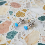 Dainty blue dot stud earrings on a textured surface