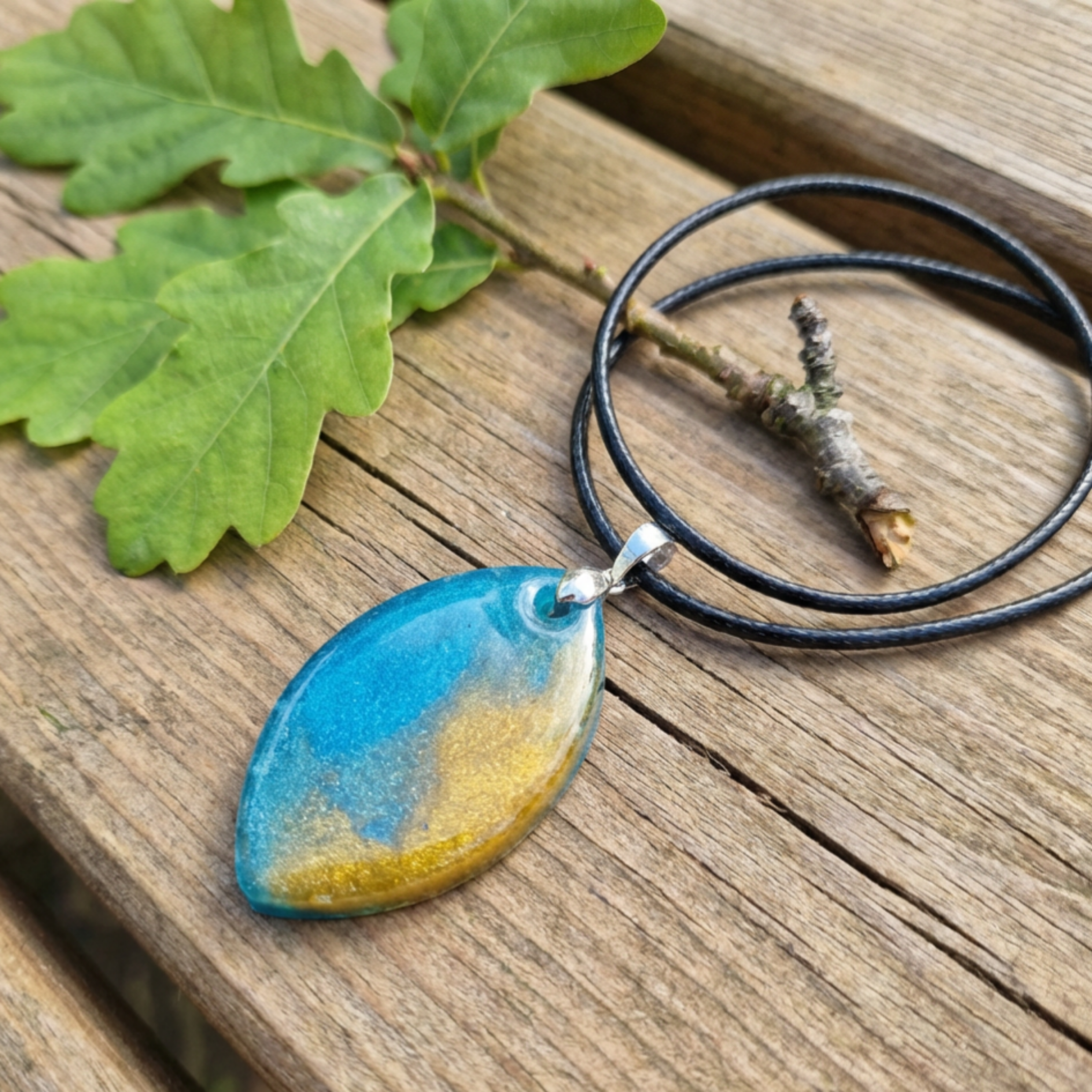 Blue Gold oval pendant with a pinch bail on a black cord on a bench