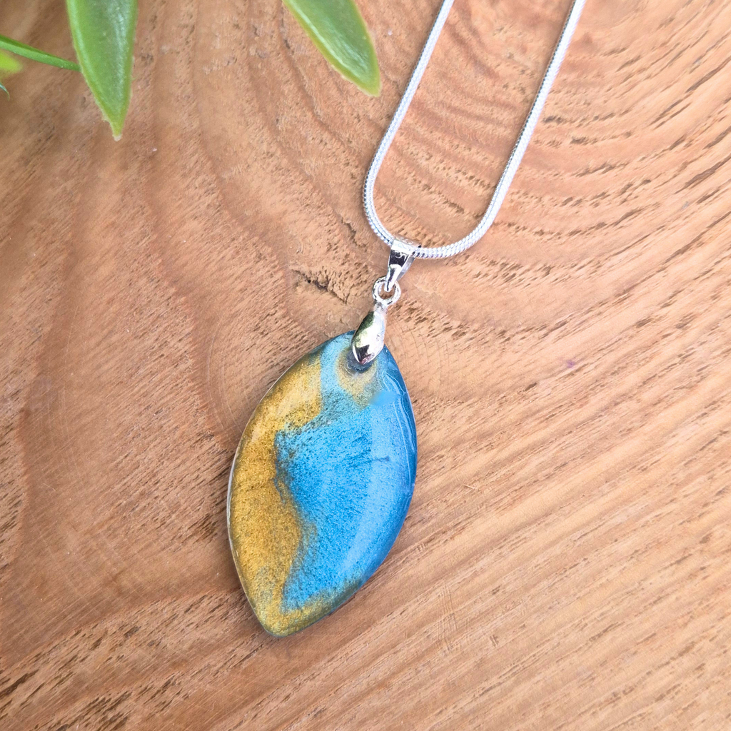 Striking blue gold oval pendant on a silver chain on a wooden surface