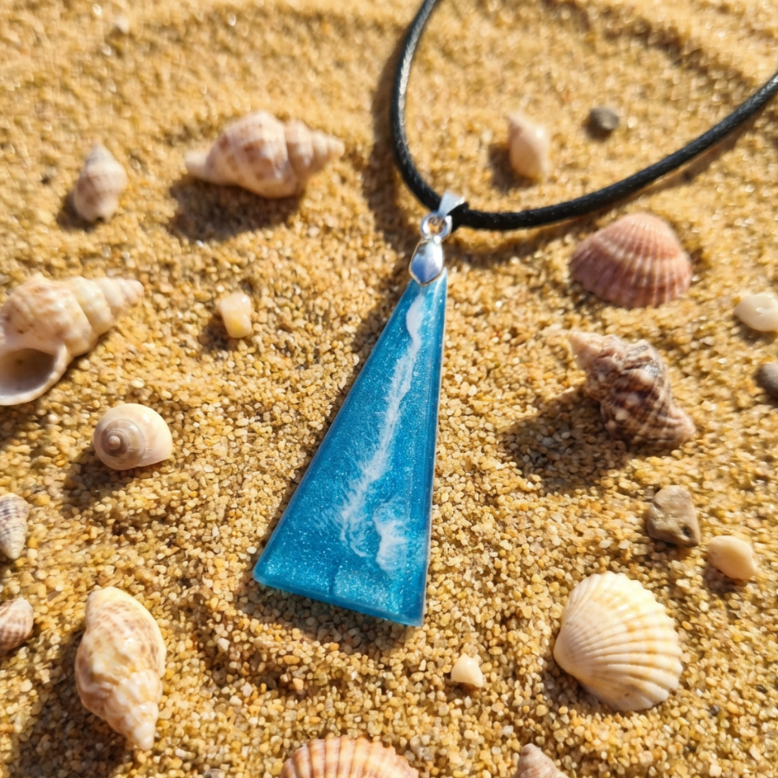 Blue triangle pendant with a white lightening stripe on sand surrounded with shells