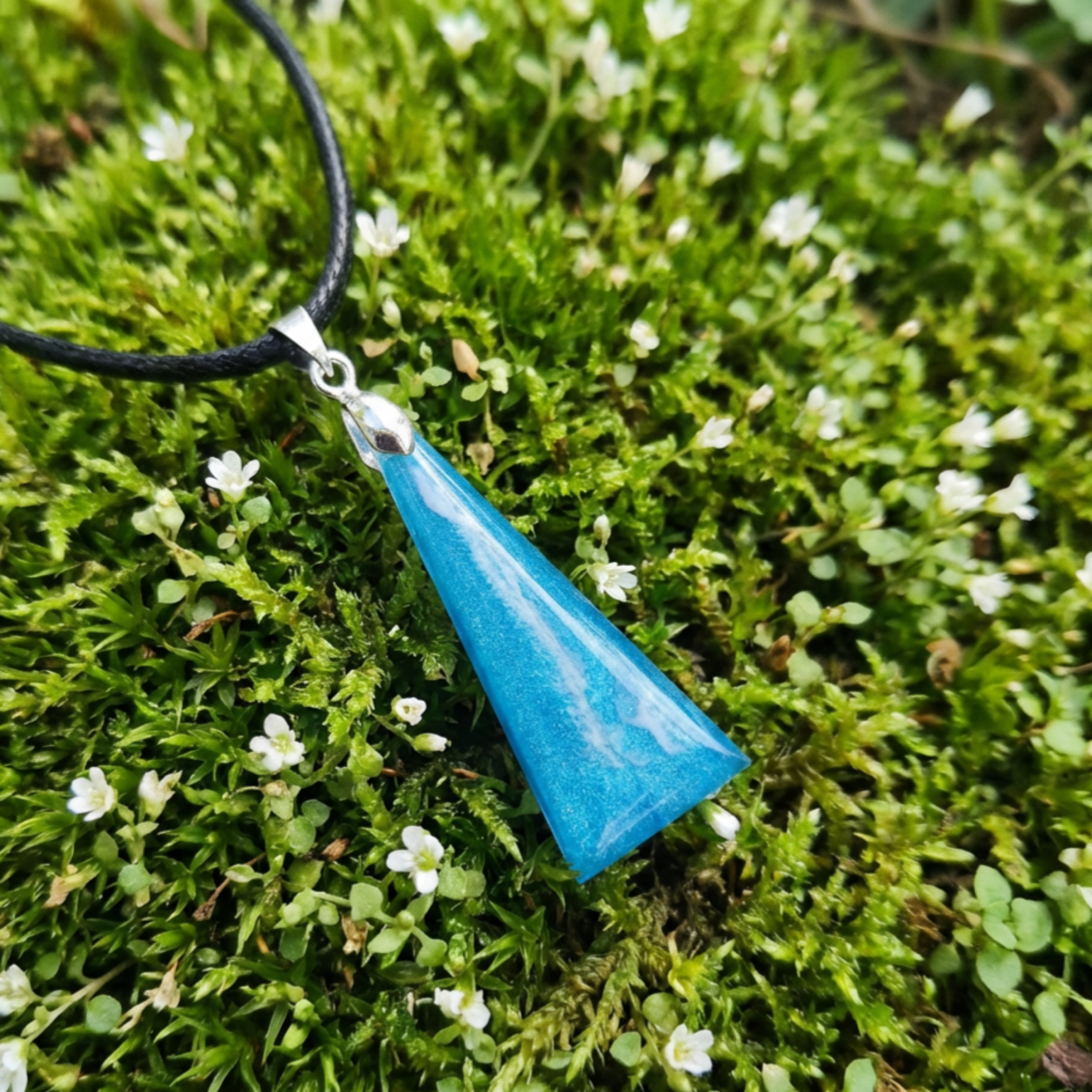 Blue pendant on a black cord against a green moss background