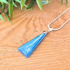 A small but bold triangle pendant on a silver pinch bail and silver chain on a wooden surface