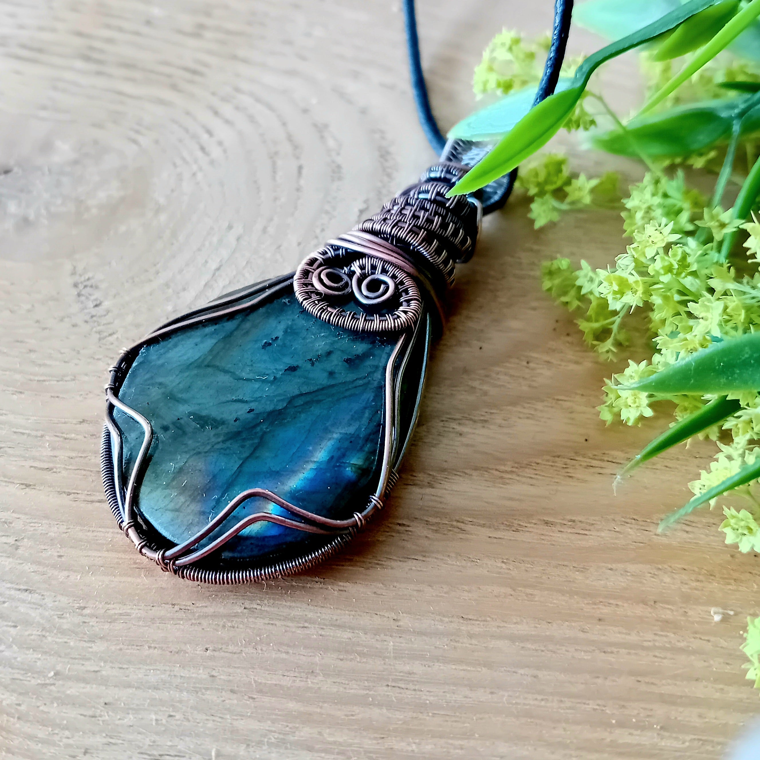 Blue pendant necklace on a wooden surface with green leaves