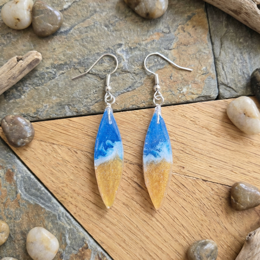 Pair of earrings with blue and gold design on a stone and wood surface