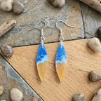 Pair of earrings with blue and gold design on a stone and wood surface