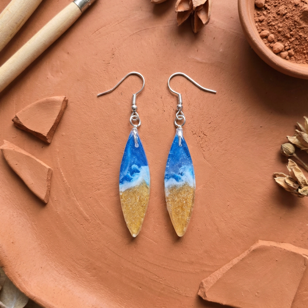 Pair of earrings with blue and gold design on a terracotta surface