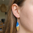 Close-up of a person wearing a blue and yellow teardrop earring with a wave design