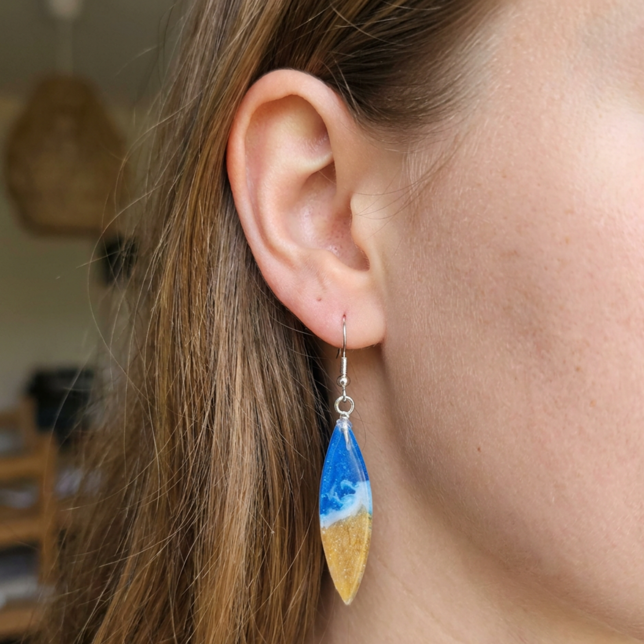 Close-up of a person wearing a blue and yellow teardrop earring with a wave design