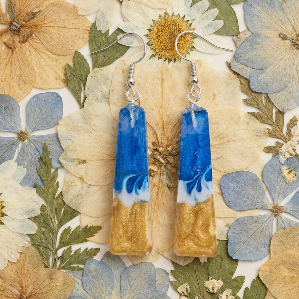 Pair of blue and gold earrings on a background of pressed flowers