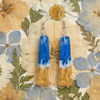 Pair of blue and gold earrings on a background of pressed flowers