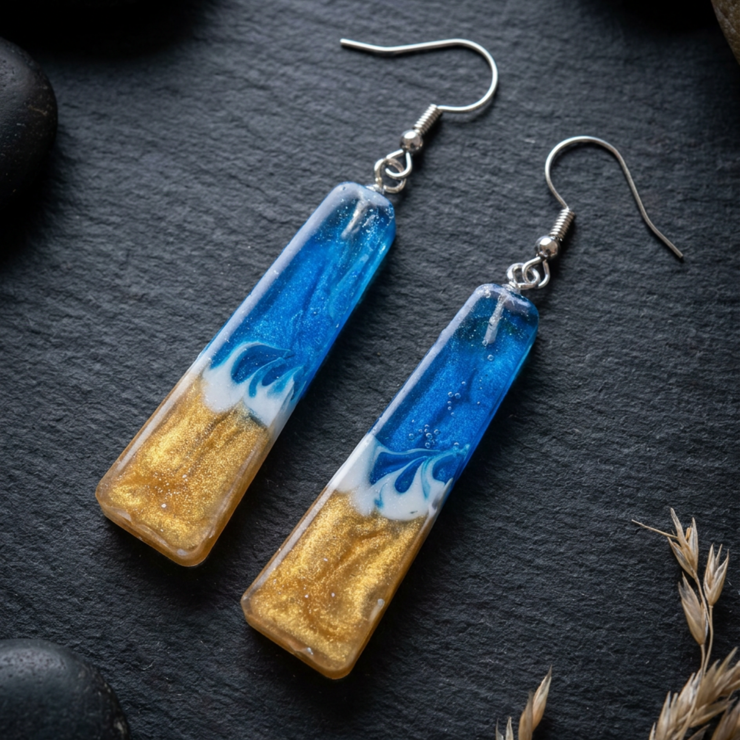 Pair of earrings with blue and gold design on a dark surface