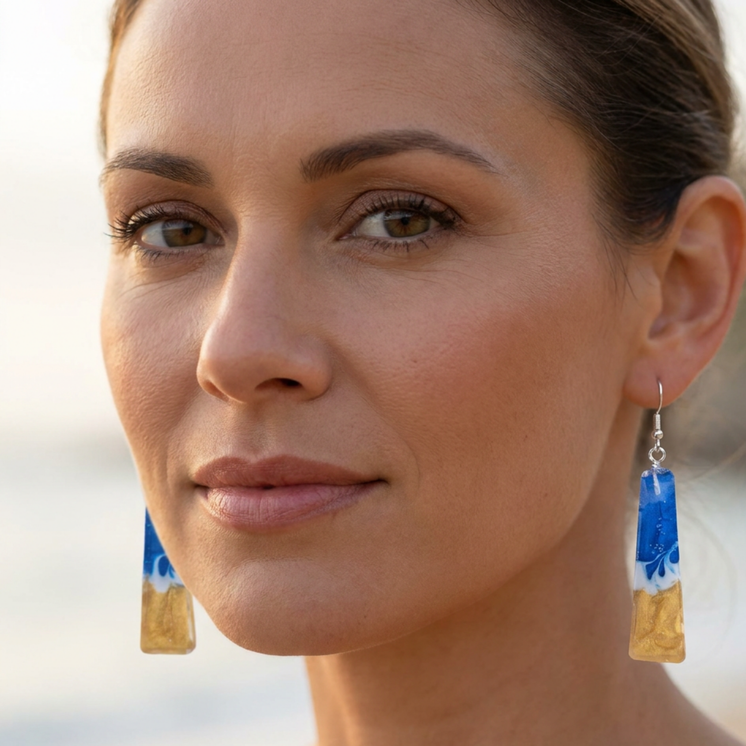 Close-up of a woman wearing blue and gold earrings with a blurred background
