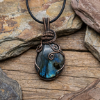 Labradorite pendant with copper wire wrapping on a wooden surface with stones