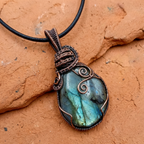 Blue gemstone pendant with copper wire wrapping on a brown stone background