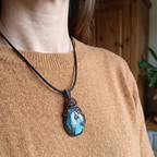 Person wearing a necklace with a blue pendant on a blurred indoor background