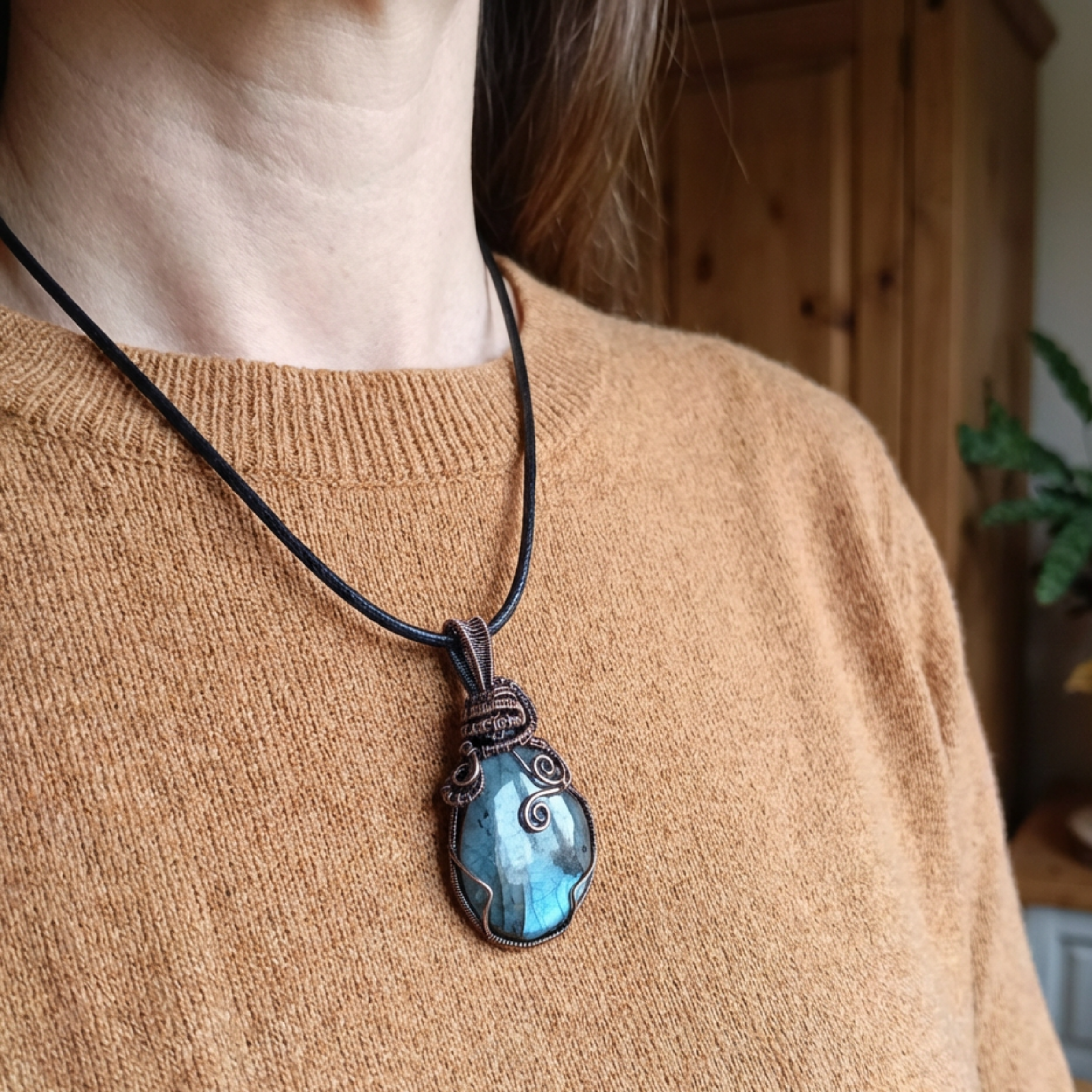 Person wearing a necklace with a blue pendant on a blurred indoor background