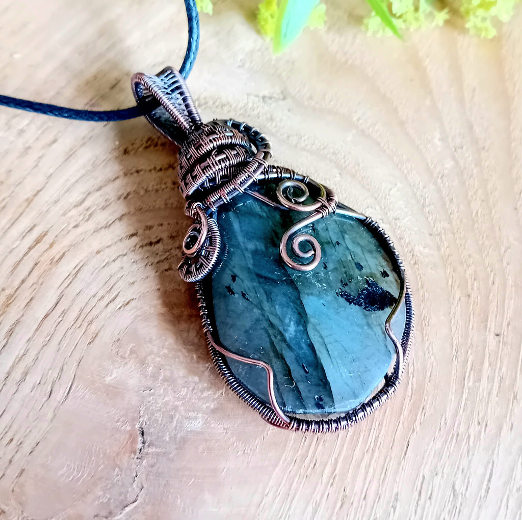 Blue stone pendant with copper wire wrapping on a wooden surface