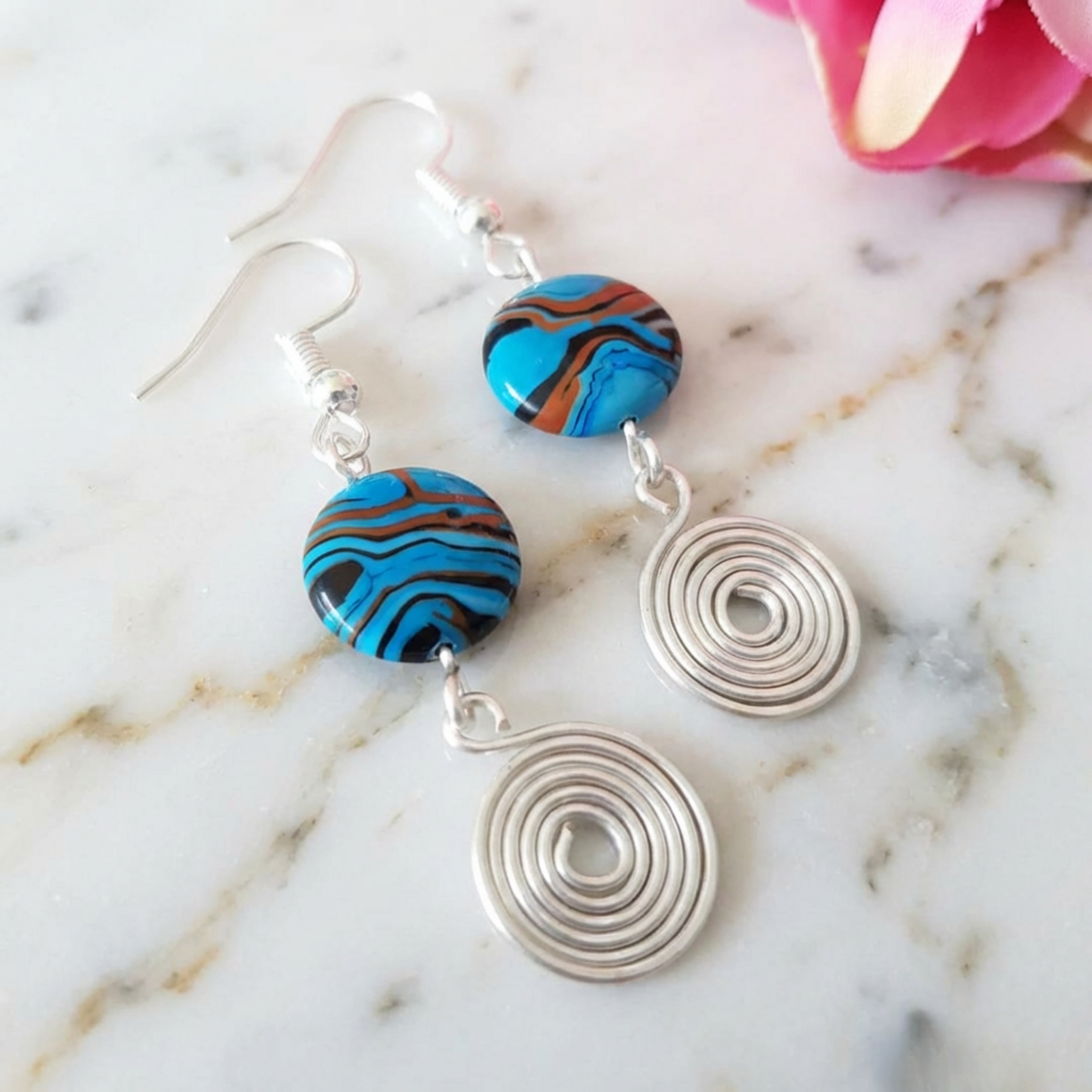 Earrings with colorful circular beads and silver spiral pendants on a marble surface.