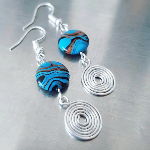 Earrings with blue and brown striped beads and silver spiral pendants on a metallic surface