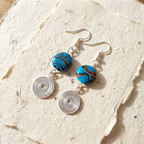 Pair of earrings with blue and brown circular beads on a textured beige surface