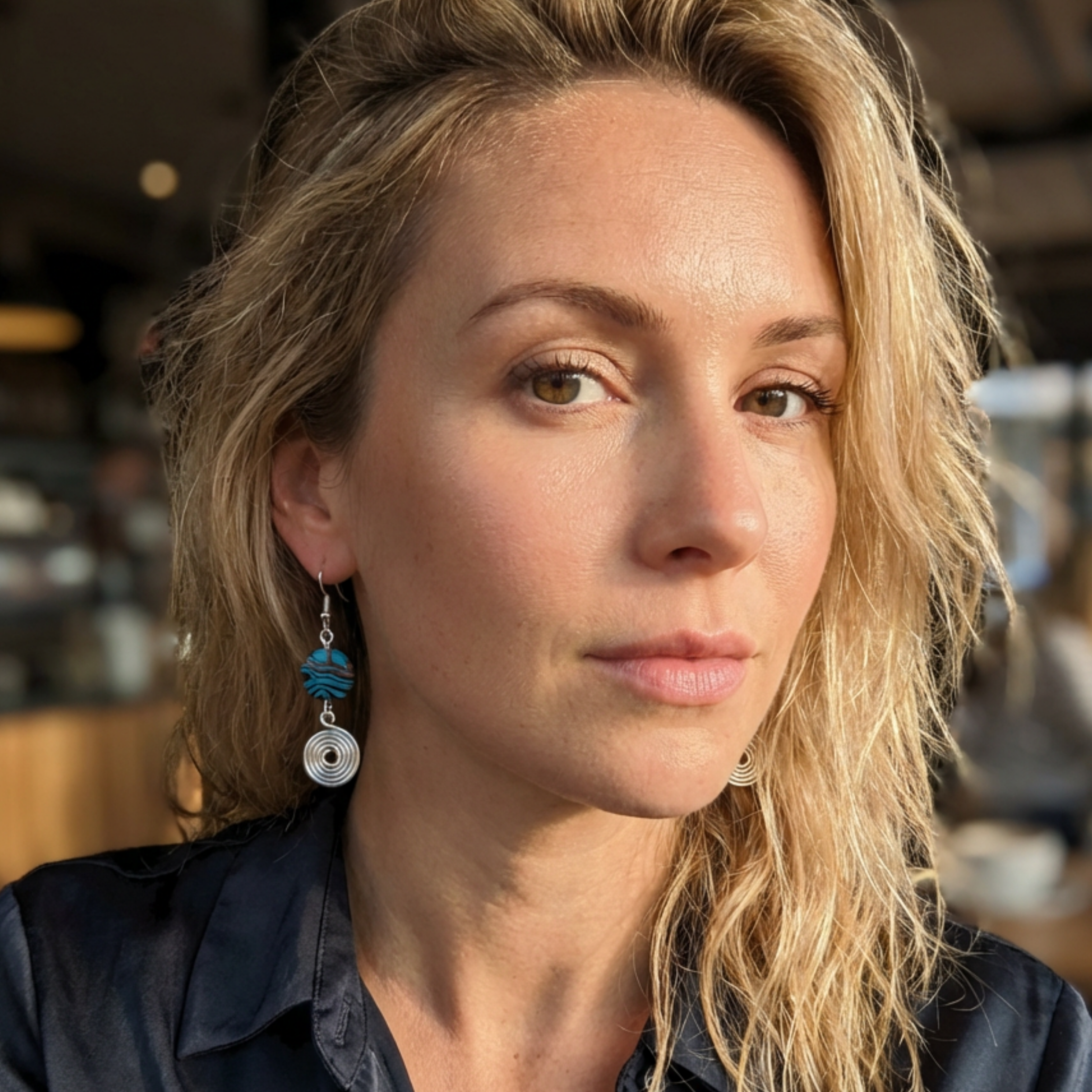 Woman with blonde hair and blue and silver earrings in an indoor setting