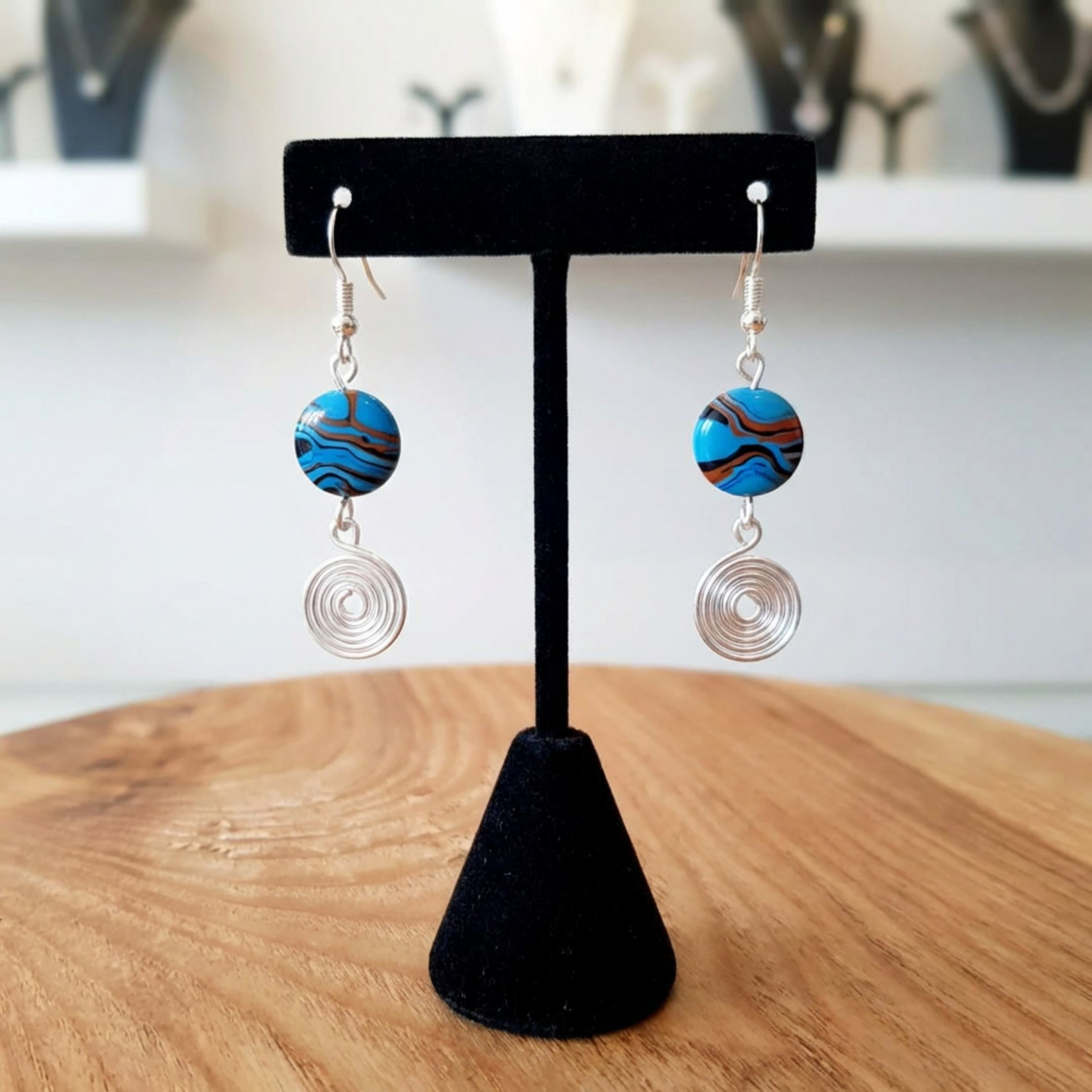 Pair of earrings with blue and brown circular designs on a black stand.