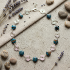 Necklace with blue and brown beads and silver spirals on a stone surface with lavender and stones.