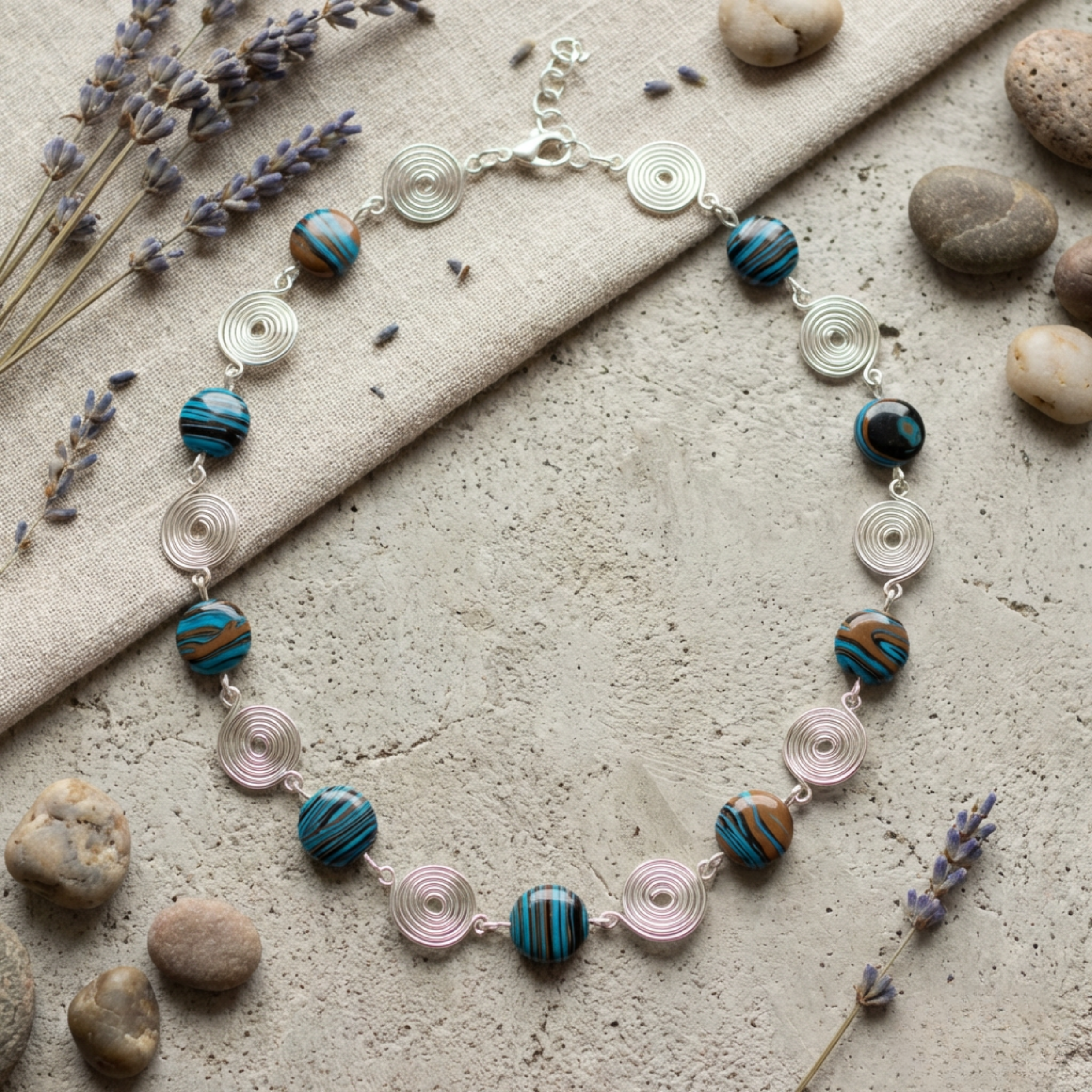 Necklace with blue and brown beads and silver spirals on a stone surface with lavender and stones.