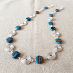 Necklace with blue and brown beads and silver spirals on a beige fabric background