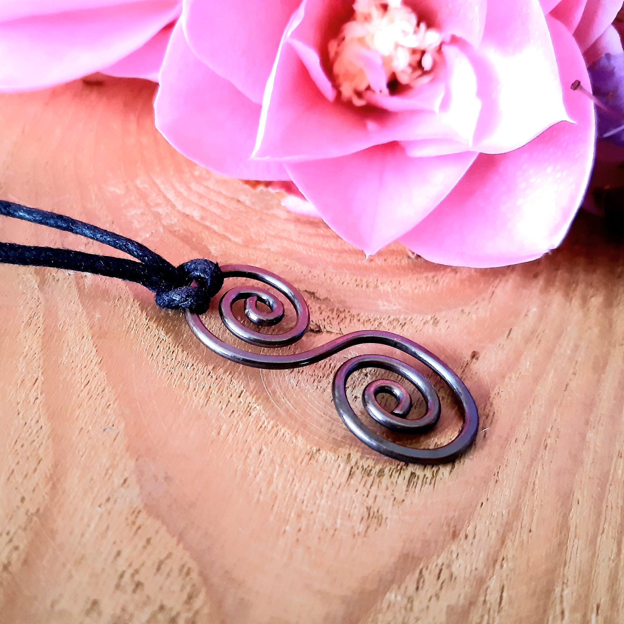 Necklace with a spiral design on a wooden surface with pink flowers in the background