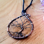Tree-shaped pendant on a wooden surface with a pink flower in the background