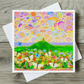 Colourful card with a landscape design featuring flowers, butterflies, and Glastonbury Tor on a wooden surface.