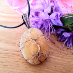 Necklace with a tree of life pendant on a wooden surface with purple flowers in the background
