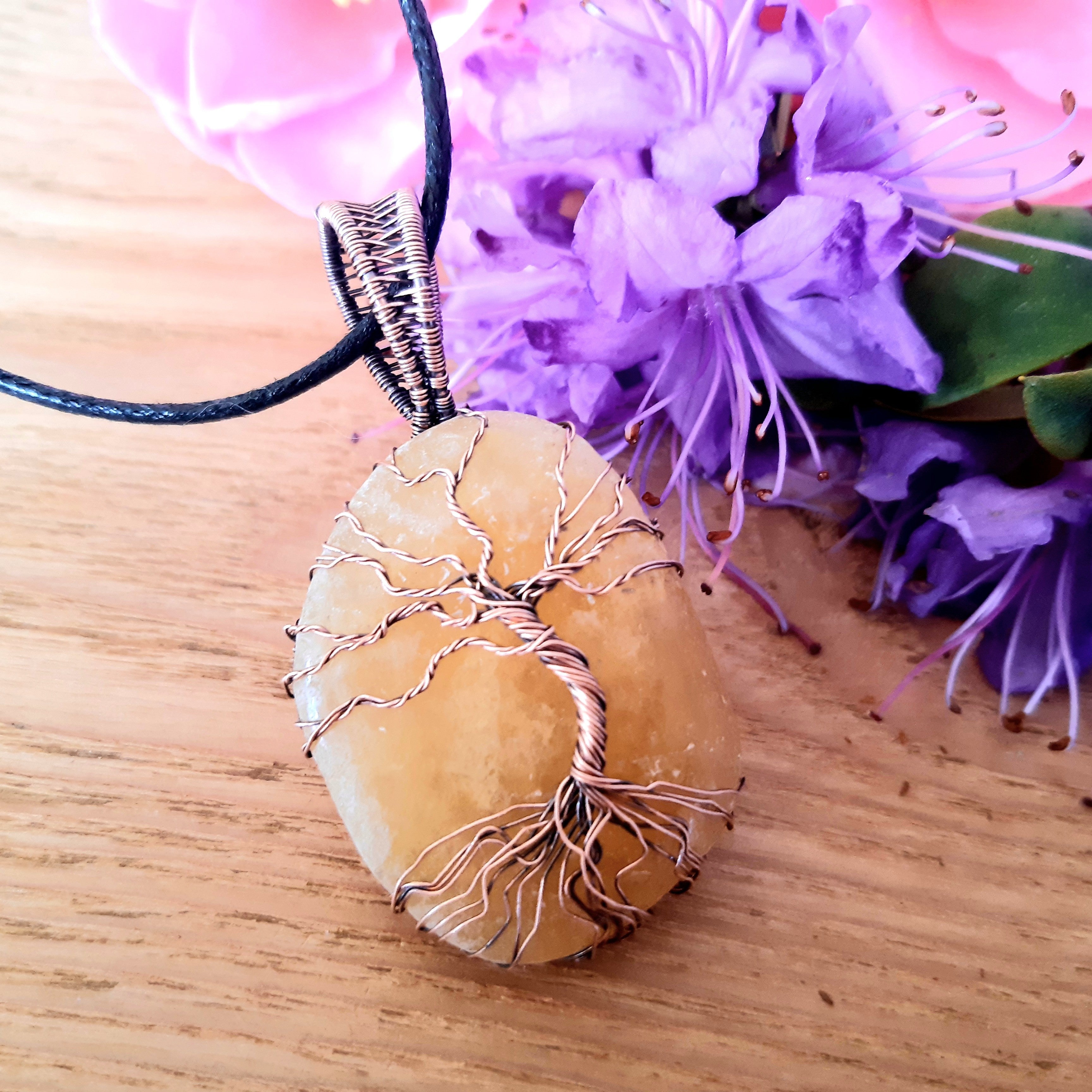 Necklace with a tree of life pendant on a wooden surface with purple flowers in the background