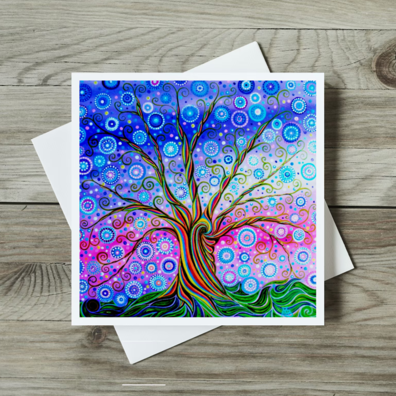 Colourful tree of life design on a greeting card with a white envelope on a wooden surface